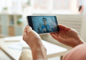 Unrecognizable person watching Asian man speaking while having online meeting on smartphone, horizontal close-up shot